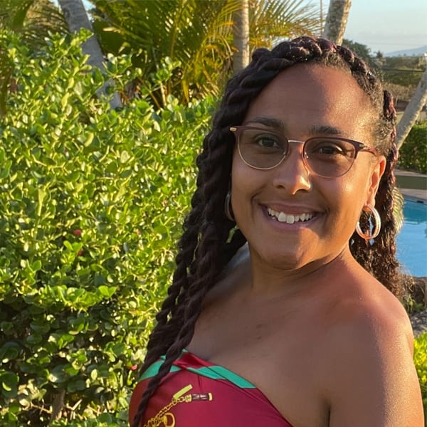 Porsche, TeamChild Legal Assistant, wears red and smiles into the camera. Behind her are green palm trees and a swimming pool.