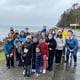 A group of TeamChild current and alumni staff and family members are gathered by the seashore on a grey day. Many wear hats and several wear face masks.