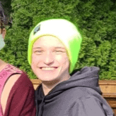 Justice, pictured outside, wears a lime-green hat and a grey sweatshirt and smiles into the camera