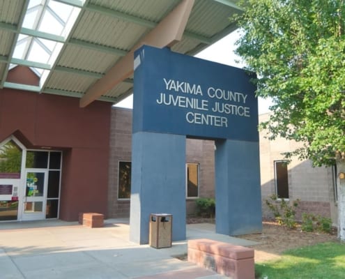Exterior of the Yakima County Juvenile Justice Center featuring brick and glass entryway and blue sign next to a tree - photo by Donald W. Meyers - Yakima Herald-Republic