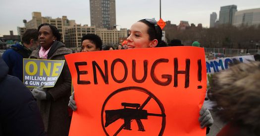 People marching with a red sign that reads ENOUGH and shows an assault rifle crossed out.