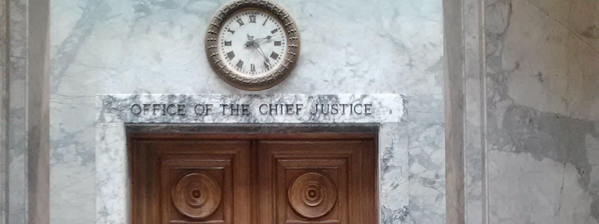 A clock is hanging on a marble wall above a sign that says Office of the Chief Justice