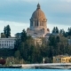 Photo of the Capitol Building in Olympia by John Callery. The building is surrounded by evergreen trees.