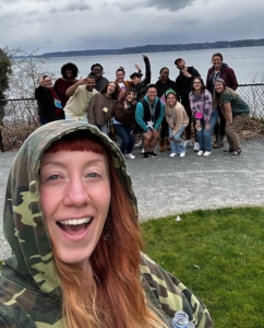 Britta takes a selfie with a group of TeamChild staff and Boardmembers behind her. Dumas Bay and a dramatic sky are in the background.